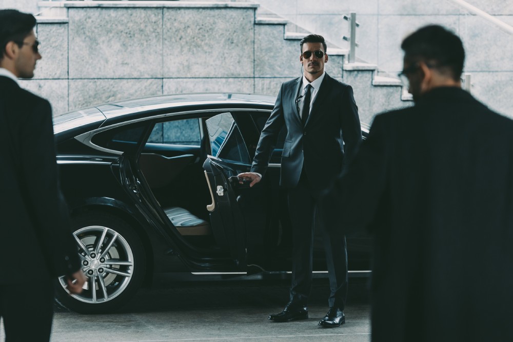 A man in suit and sunglasses standing next to a car.